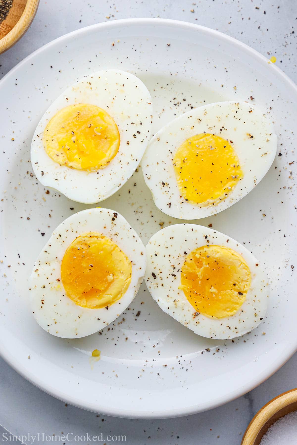 Vertical image of Air Fryer Hard Boiled Eggs peeled and cut, topped with salt and pepper, on a white plate.