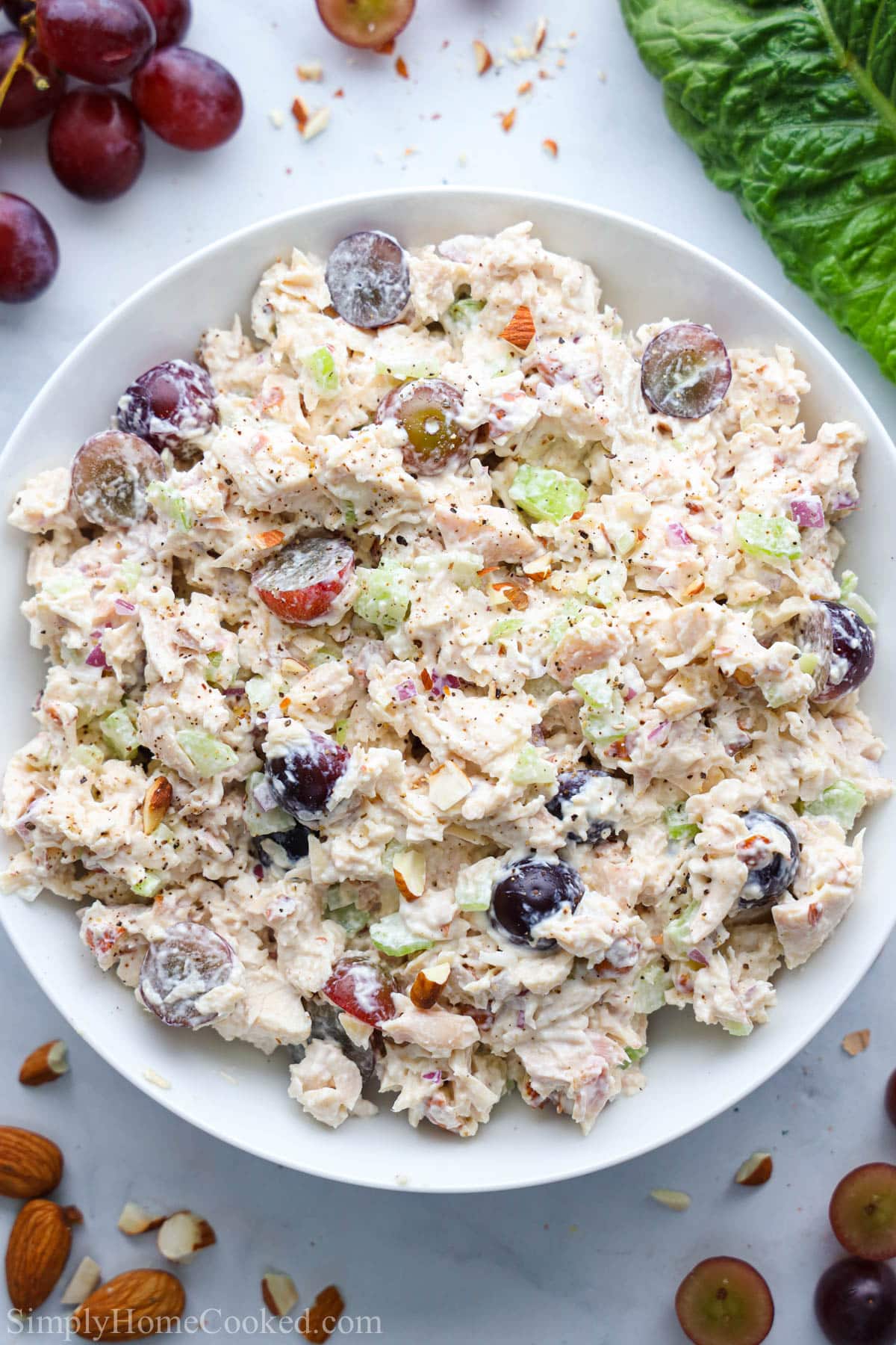 This quick and easy chicken lettuce wraps recipe is made with cubed rotisserie chicken, crunchy grapes, toasted almonds, and a simple creamy dressing. #chickensalad #chickenwrap #lettucewraps #chickenlettucewrap #healthylettucewrap #ketolettucewrap Chicken Salad with Grapes in a white bowl with grapes and lettuce nearby