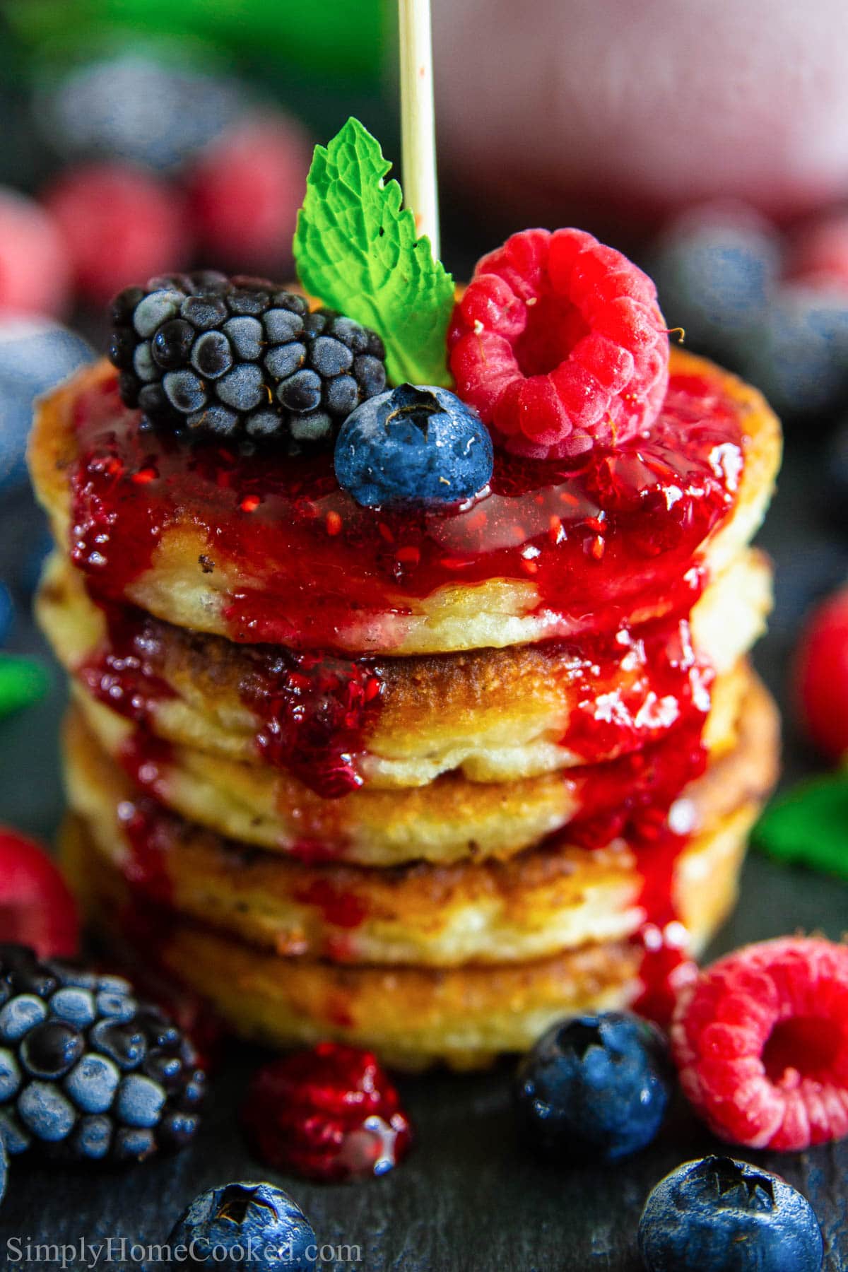 Cottage cheese pancakes make a delicious dessert or tasty breakfast. Fluffy, fruity, and not too sweet, these mini pancakes will become a family favorite. #minipancakes #pancakes #cottagecheesepancakes #blinchiki #breakfastfordessert A stack of Cottage Cheese Pancakes with raspberry sauce and fresh berries.