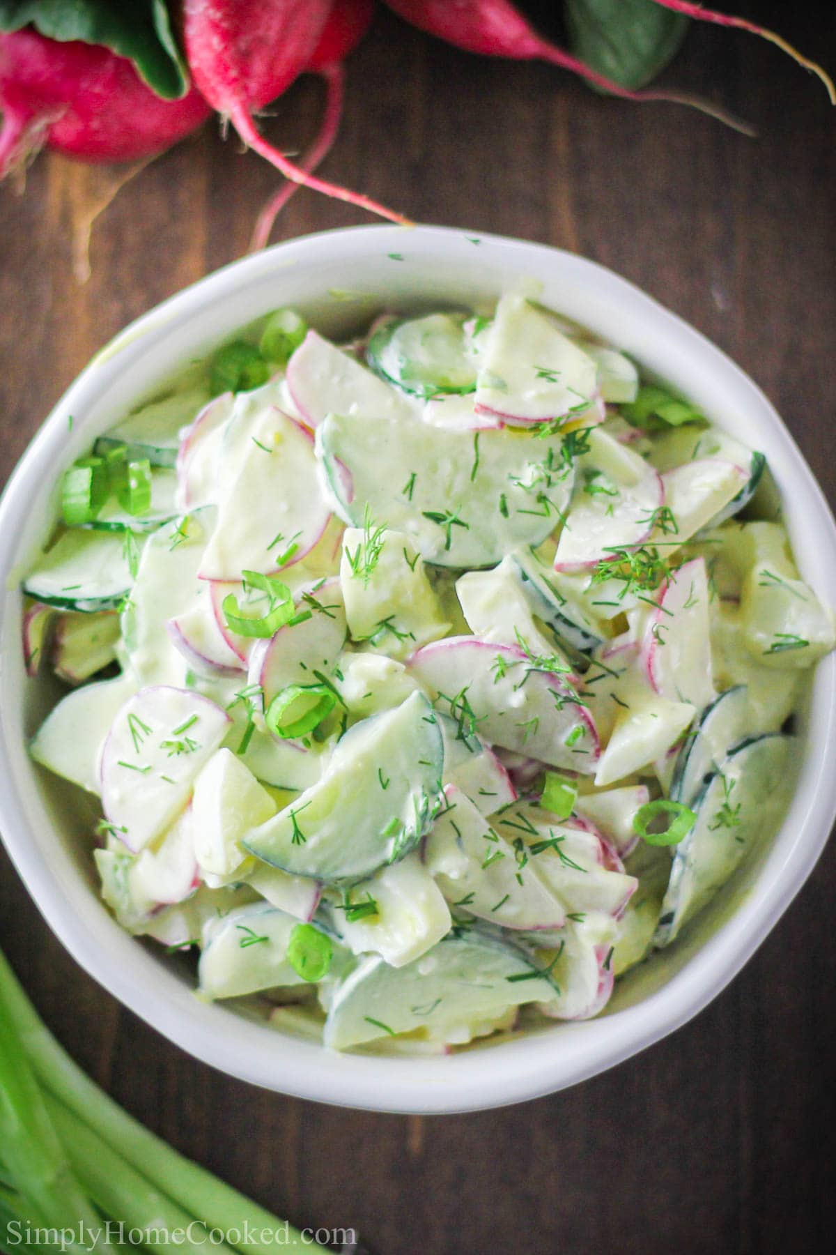 Overhead view of Cucumber Radish Salad in a white bowl with dill on top.
