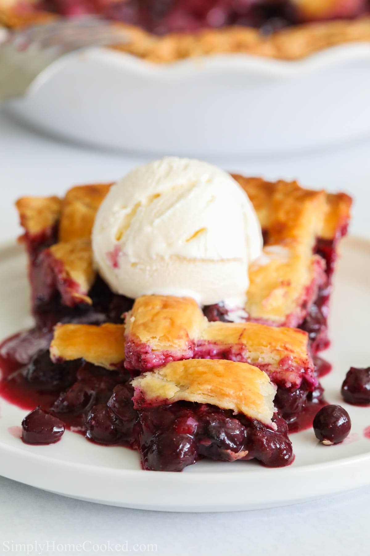Hands down the best blueberry pie recipe that's made with a flakey homemade pie crust and fresh summer blueberries. It will become your favorite pie recipe! #blueberrypie #pierecipe #homemadepie #bestpie #piecrust Blueberry Pie slice with a scoop of vanilla ice cream on top on a white plate