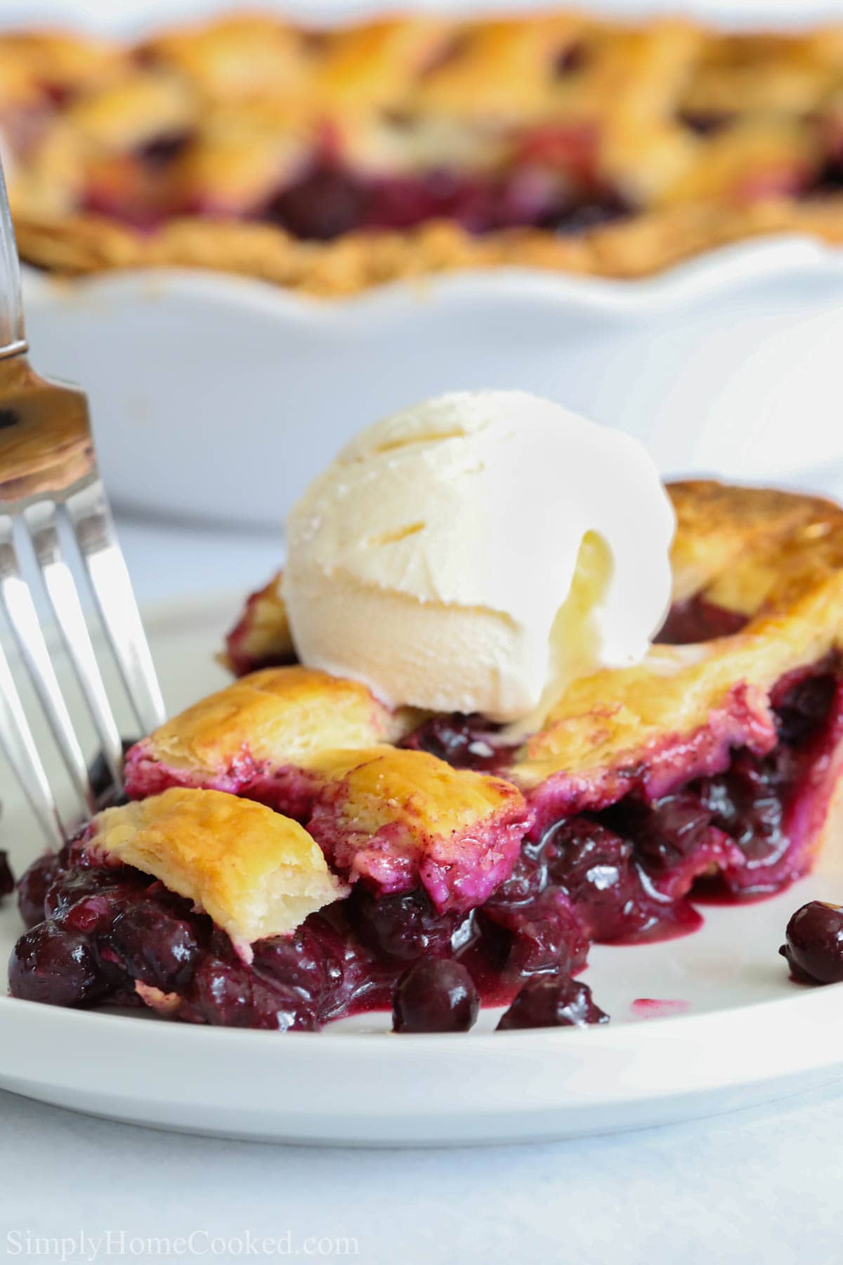 Blueberry Pie slice with a scoop of vanilla ice cream on top on a white plate with a fork