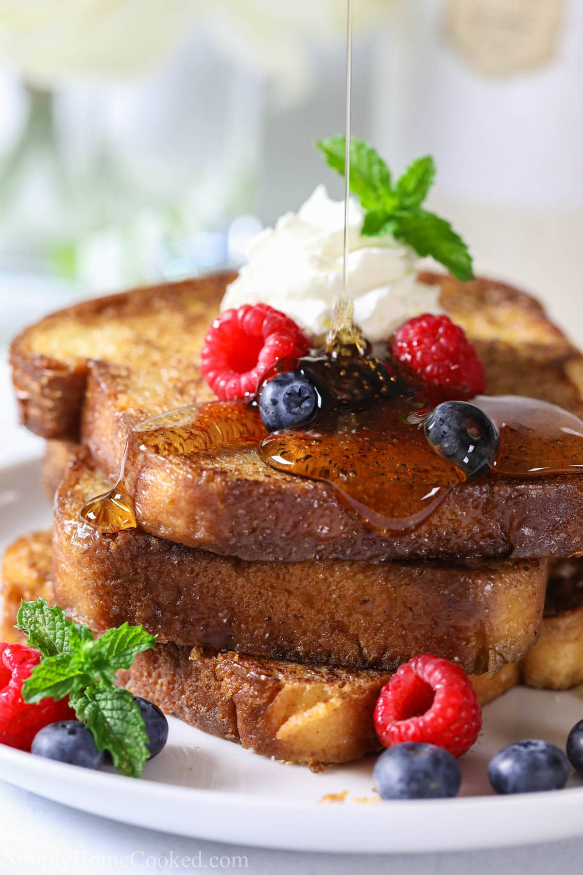 This thick, fluffy, and buttery brioche French toast is the ultimate way to enjoy a stack of homemade french toast. And the best part, it's so easy to make! #briochefrenchtoast #frenchtoast #bestfrenchtoast #briocherecipe #briochedessert Syrup drizzling on a stack of Brioche French Toast on a plate with fresh berries and whipped cream