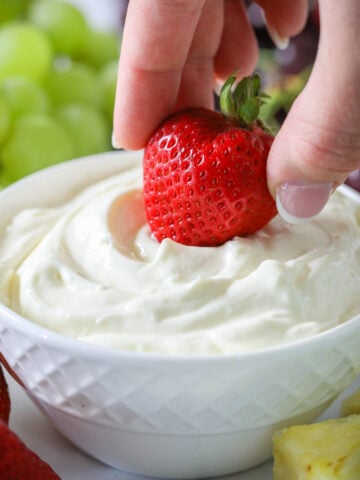 Hand dipping a strawberry into Cream Cheese Fruit Dip in a white bowl