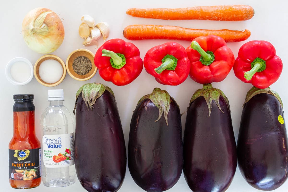 Ingredients for Eggplant Salad, including eggplant, red bell peppers, garlic, onion, carrots, salt, pepper, sugar, vinegar, and sweet chili sauce.