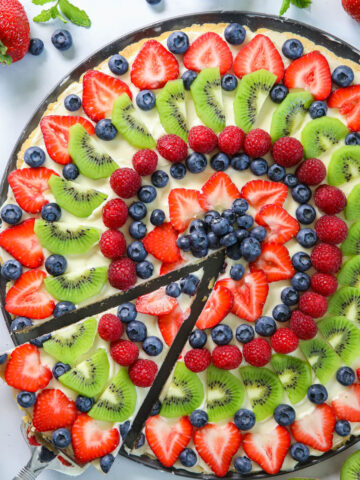 Fruit Pizza with a slice being lifted out and strawberries and kiwis nearby