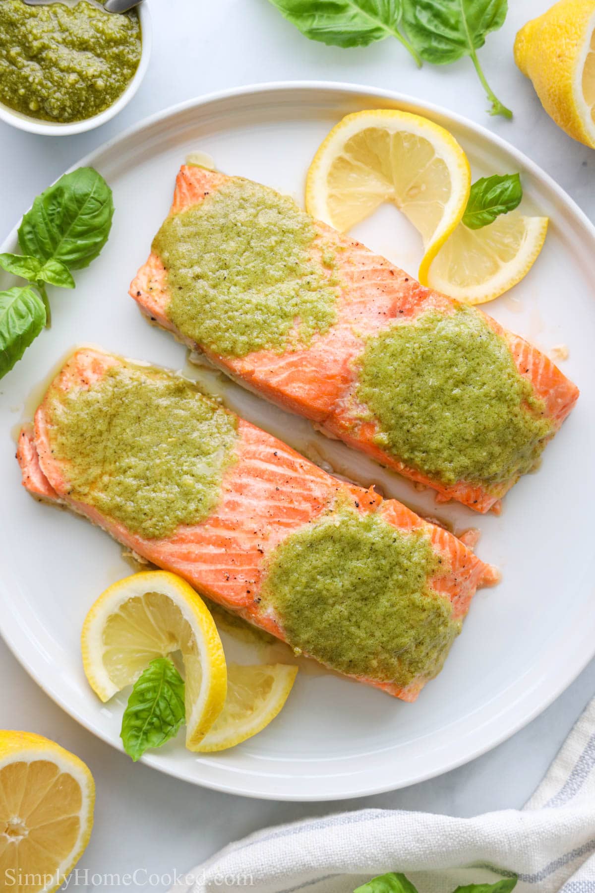 Baked salmon fillets with fresh pesto butter on top. A quick salmon dinner done in 15 minutes from start to finish. #bakedsalmon #Salmondinner #pestosalmon #bakedfish Pesto Salmon filets on a white plate with basil and lemon slices