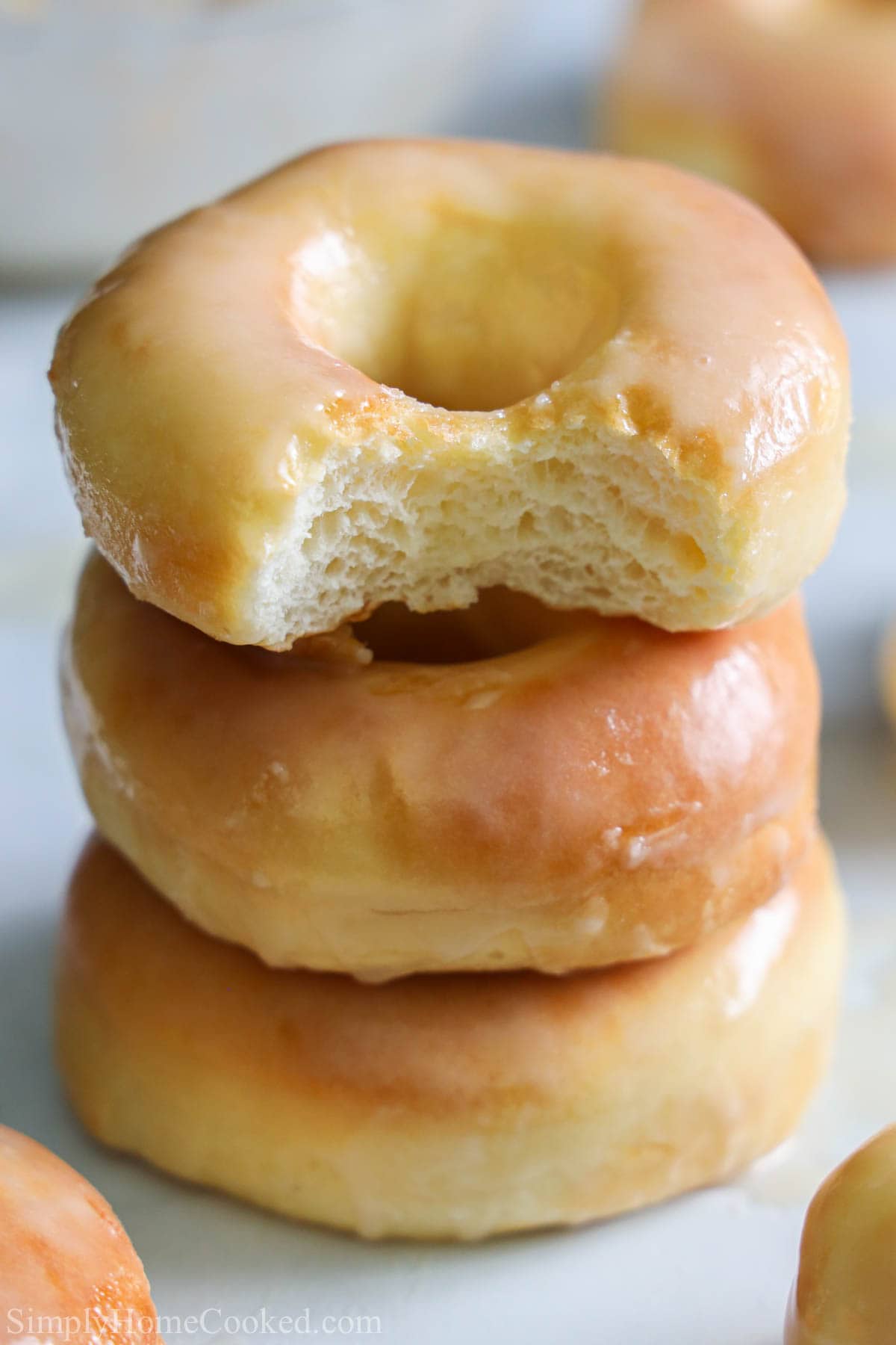 These Glazed Air Fryer Donuts (from scratch) are the perfect thing for your sweet tooth. Moist, fluffy, & light, they will melt in your mouth. #airfryerdonutrecipe #glazeddonutrecipe #glazedairfryerdonutrecipe #airfryerglazeddonutrecipe Stack of Glazed Air Fryer Donuts, the top one missing a bite