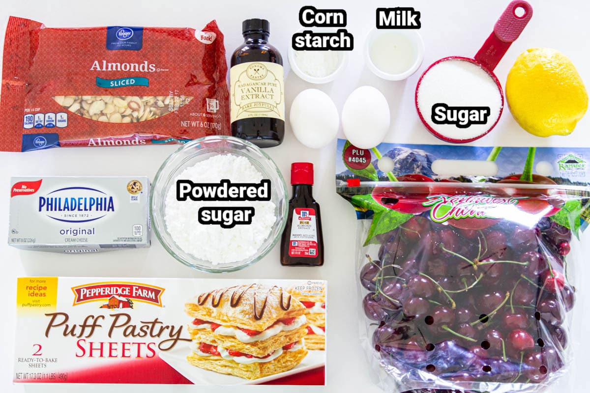 Ingredients for Cherry Danish, including almonds, fresh cherries, sugar, lemon, egg, cornstarch, milk, almond and vanilla extracts, powdered sugar, cream cheese, and puff pastry.