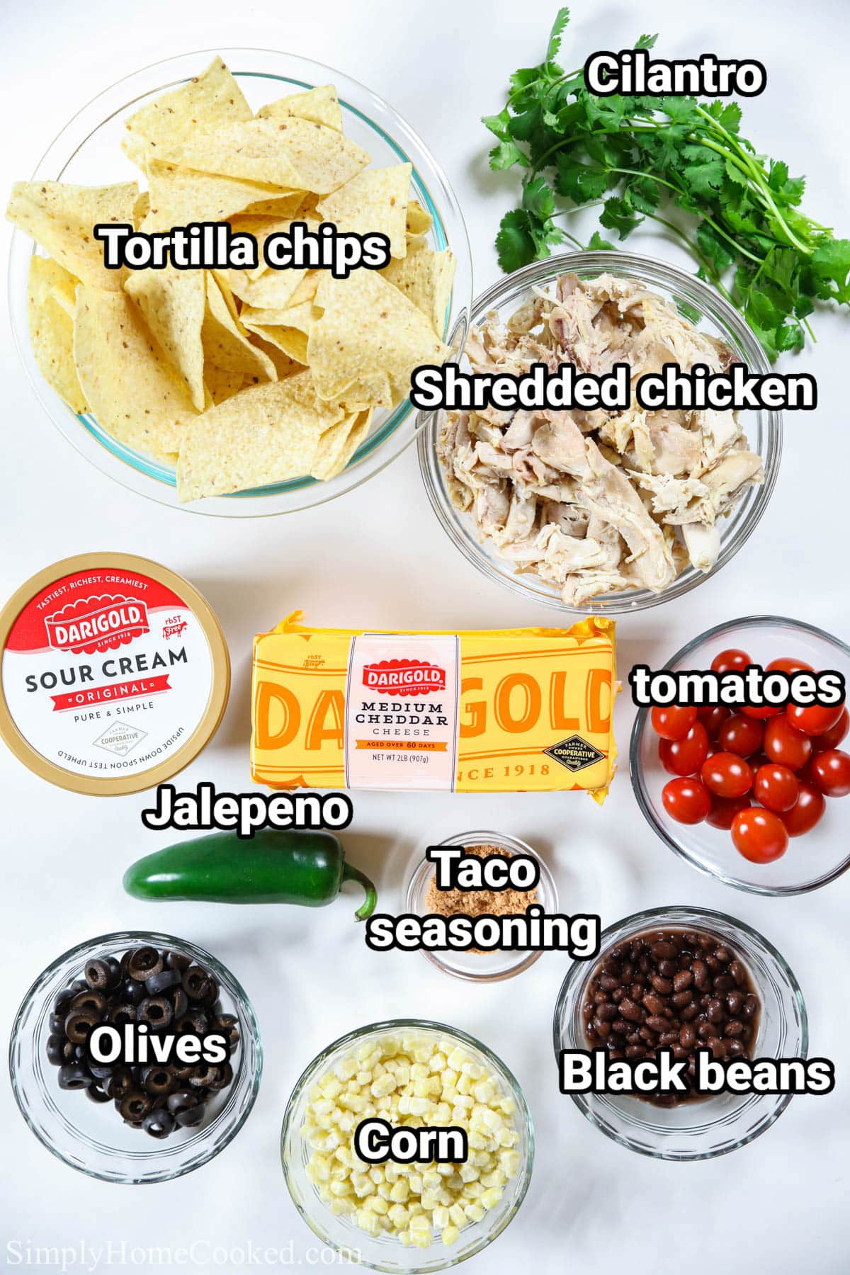 Ingredients for Loaded Chicken Nachos, including tortilla chips, shredded chicken, cheese, taco seasoning, sour cream, cilantro, tomatoes, jalapenos, corn, olives, and black beans.