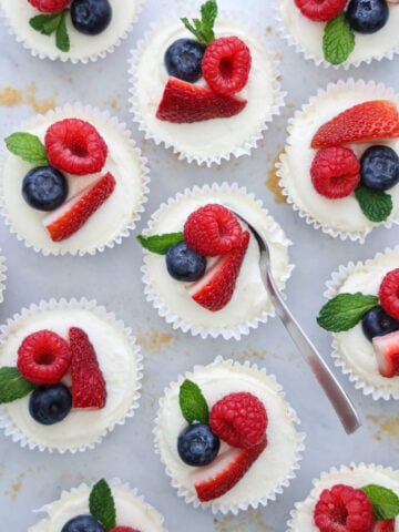 Overhead of No Bake Mini Cheesecakes topped with fresh berries and a spoon scooping into one of them