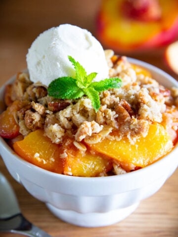 Peach Crisp in a white bowl with a scoop of vanilla ice cream on top with a mint leaf