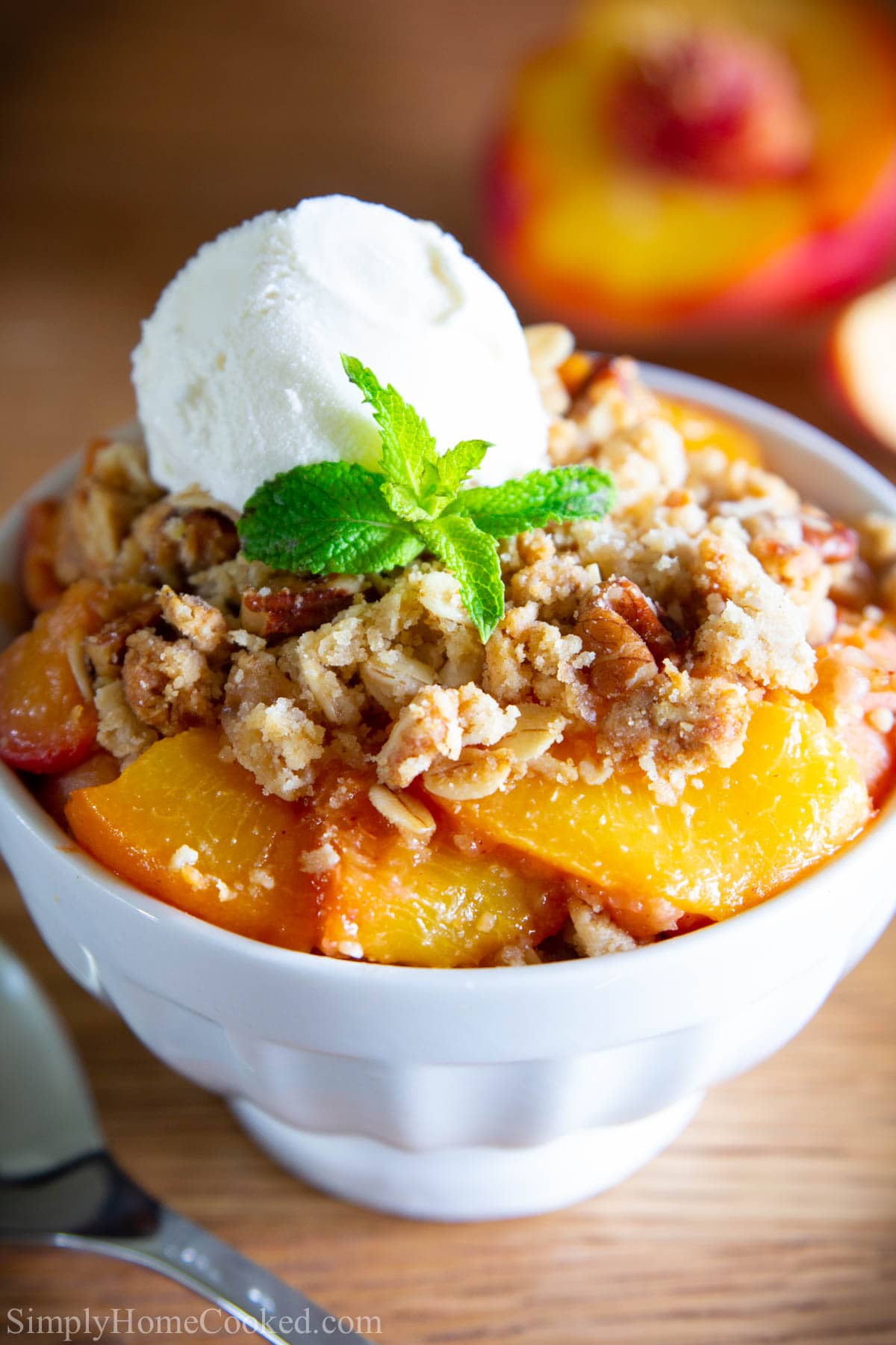This EASY Peach Crisp Recipe is unbelievably delicious! Bursting with flavor from the fresh peaches that are covered with a sweet streusel oat topping! Topped with some ice cream, this summer dessert can really be enjoyed year-round. #peachcrisp #crisprecipe #peachrecipe #bakedpeaches Peach Crisp in a white bowl with a scoop of vanilla ice cream on top with a mint leaf