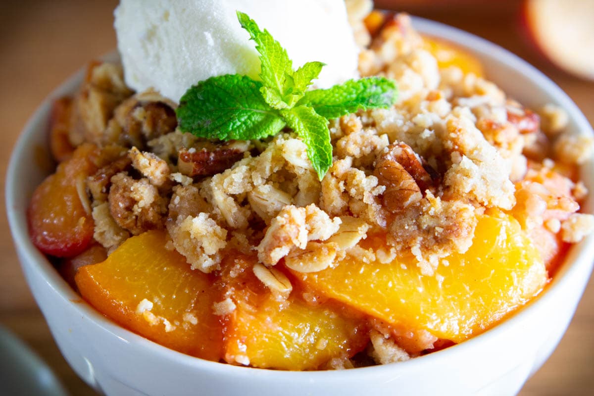Peach Crisp in a white bowl and topped with ice cream nd mint leaves.
