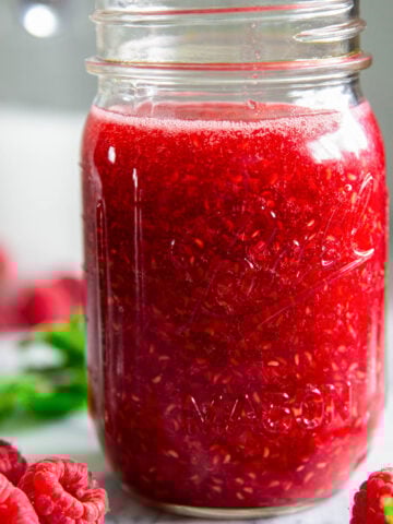 Mason jar full of Raspberry Sauce with fresh raspberries nearby