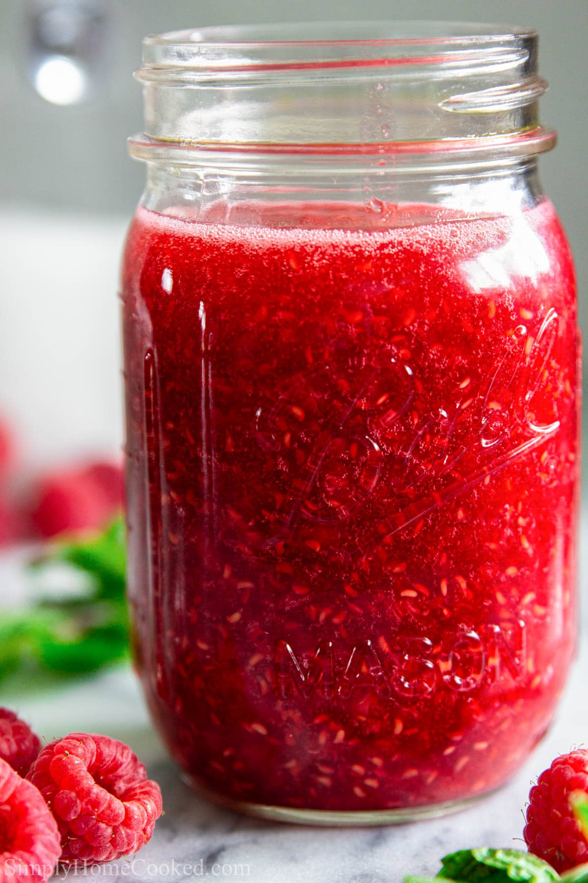 This Fresh Raspberry Sauce Recipe is a perfect simple fruit sauce that blends together quickly and is ideal for topping ice cream, cakes, and desserts. #raspberrysauce #freshraspberrysauce #fruitsauce #raspberryjam #rasoberrysyrup Mason jar full of Raspberry Sauce with fresh raspberries nearby