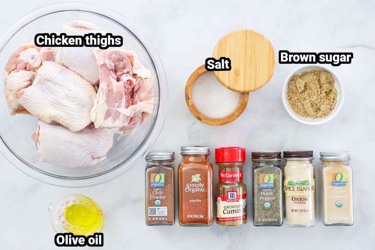Ingredients for Smoked Chicken Thighs, including chicken thighs, salt, brown sugar, olive oil chili powder, paprika, cumin, pepper, onion powder, and garlic powder. 