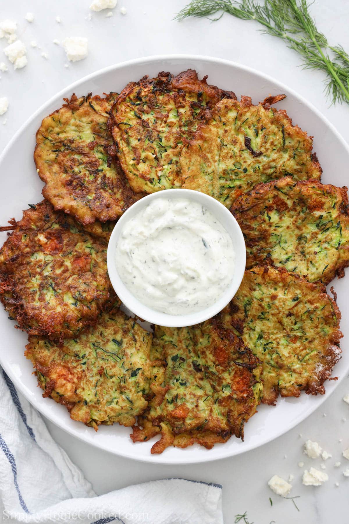 Zucchini Fritters surrounded in a bowl of tzatziki sauce on a white plate