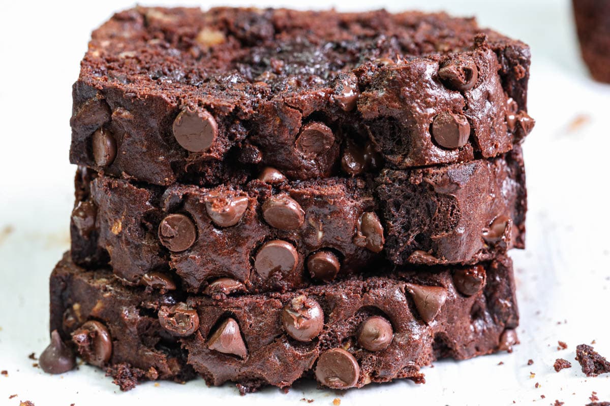 This Double Chocolate Banana Bread Recipe is so sweet and decadent, you're going to love it. Moist and delicious, it's the perfect after-dinner dessert or tasty afternoon snack. #bananabread #bananabreadrecipe #chocolatebananabread #chocolatebananabreadrecipe Slices of Double Chocolate Banana Bread piled on each other