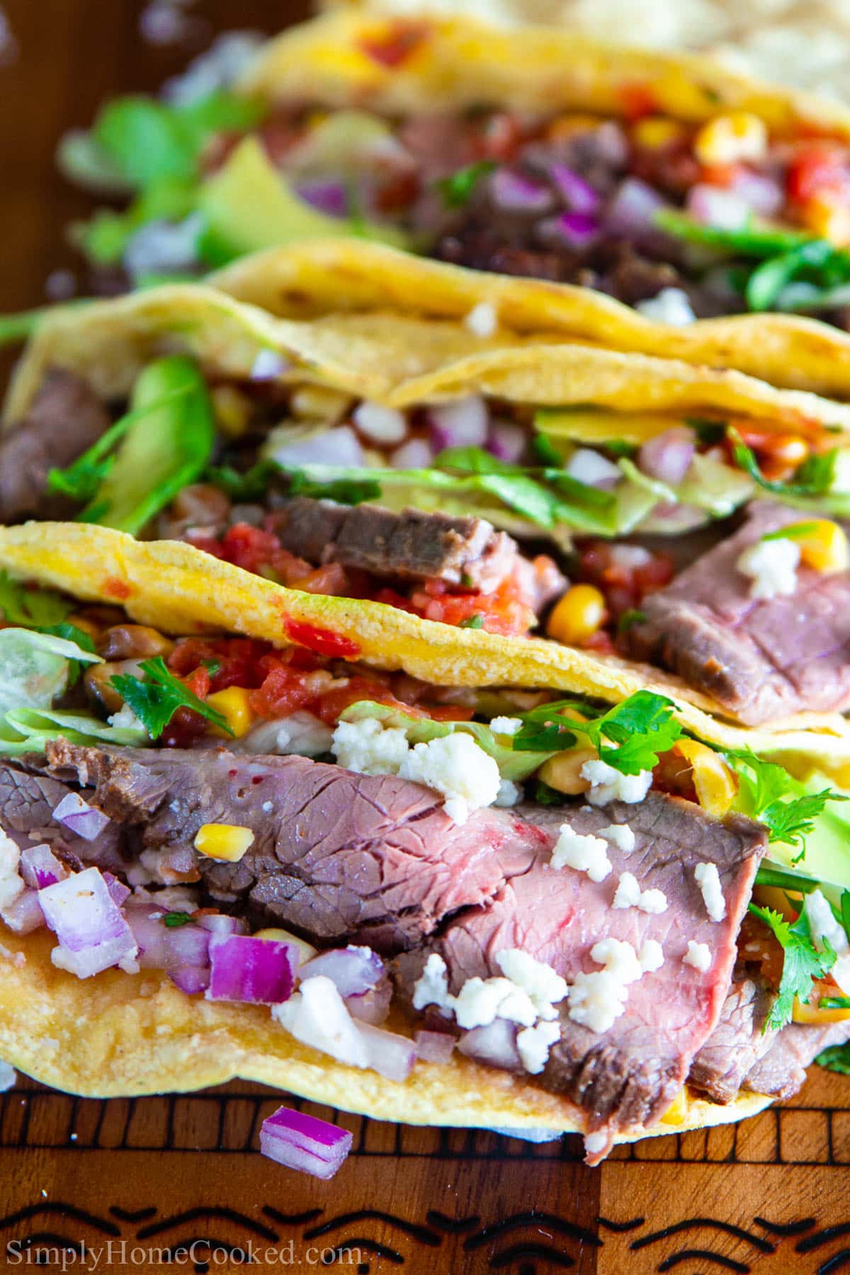 This Delicious Flank Steak Taco Recipe is simple and packed full of vibrant flavors. Follow this step by step recipe to create irresistible steak tacos! #steaktacos #streettacos #beeftacos #grilledtacos #easytacos #tacorecipe Flank Steak Tacos lined up