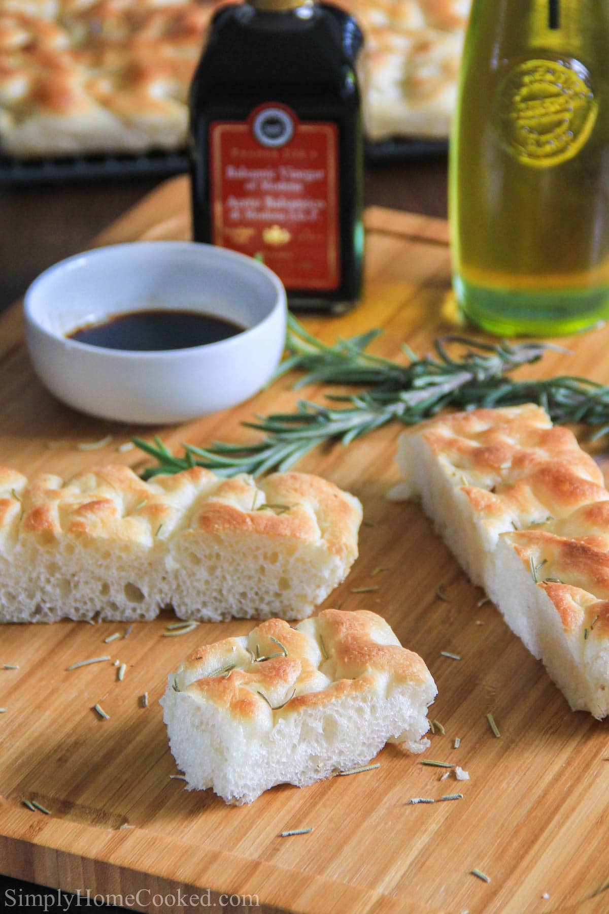 Focaccia Bread slices on a cutting board with rosemary sprigs, oil, and balsamic vinegar.