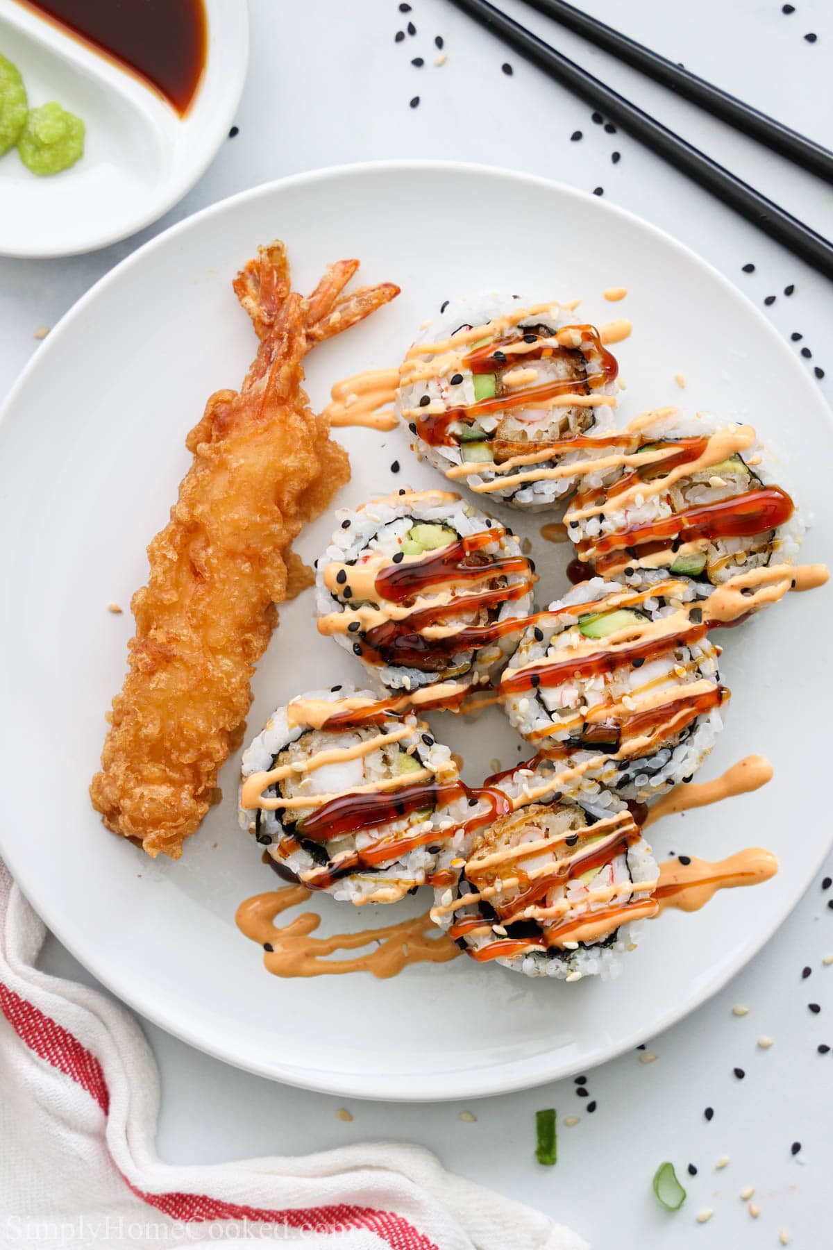 Sliced Dynamite Roll with unagi sauce and spicy mayo drizzled on top next to some shrimp tempura