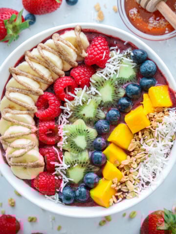 Acai Bowl topped with fresh fruit, coconut flakes, granola, honey, and nut butter, with strawberries and honey nearby.