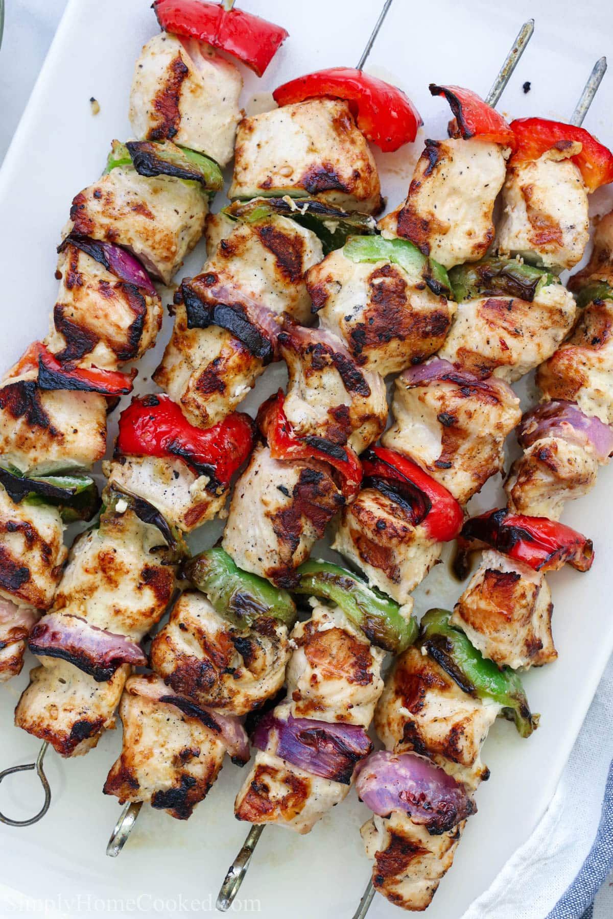 These Grilled Chicken Kabobs are so easy to make and delicious. Just marinate the meat overnight and then grill them up for a tasty dinner on a summer night. #grilledchickenkabobs #chickenkabobs #bestkabobs #easykabobrecipe Grilled chicken kabobs with red onion and green and red pepper pieces on metal skewers