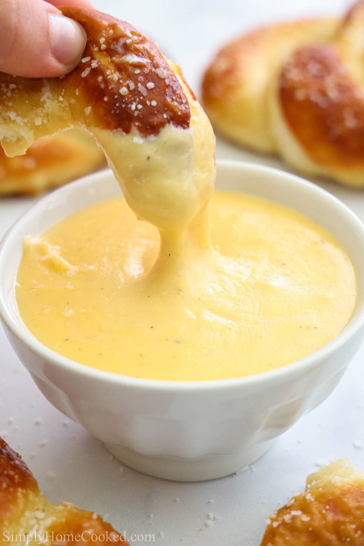 Hand dipping a piece of soft pretzel into a bowl of Pretzel Cheese Dip.