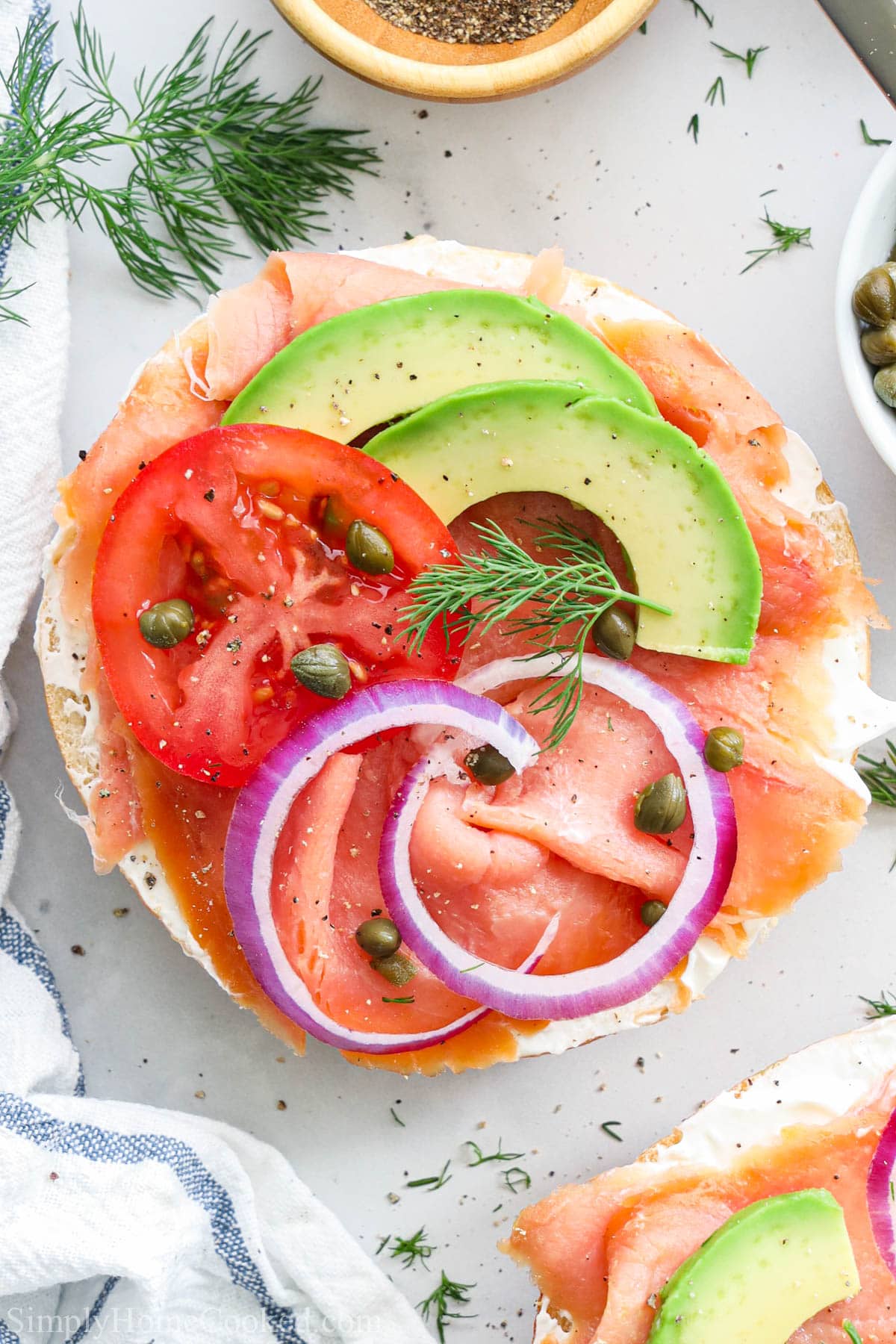 An easy and delicious smoked salmon bagel. This recipe is loaded with cream cheese and healthy toppings. #salmonbagel #smokedsalmon #salmonbreakfast #breakfastbagel #smokedsalmontoast Smoked Salmon Bagel topped with onion, capers, tomato, dill, and avocado.