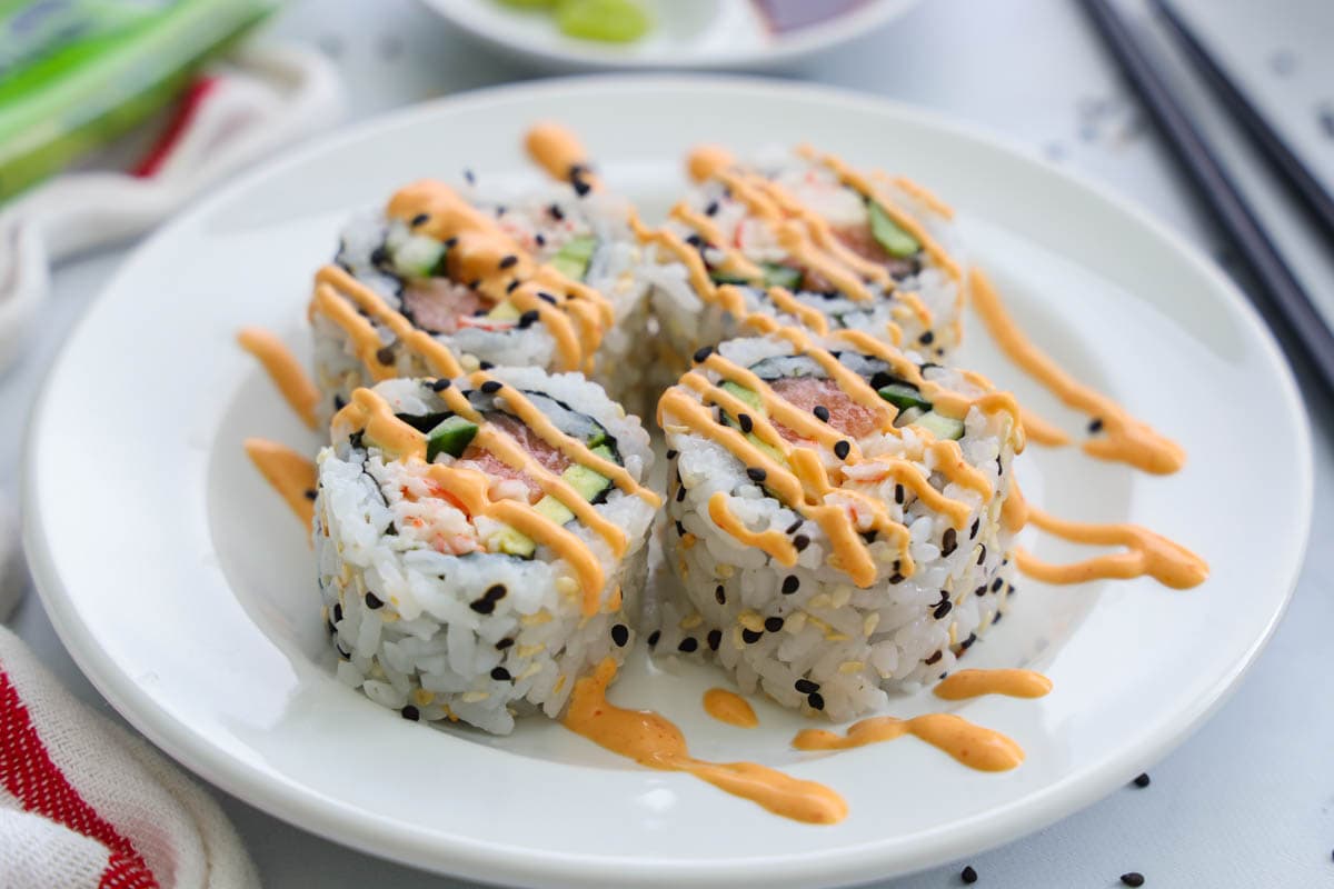 Spicy Salmon Roll cut up on a white plate with spicy mayo drizzled on top
