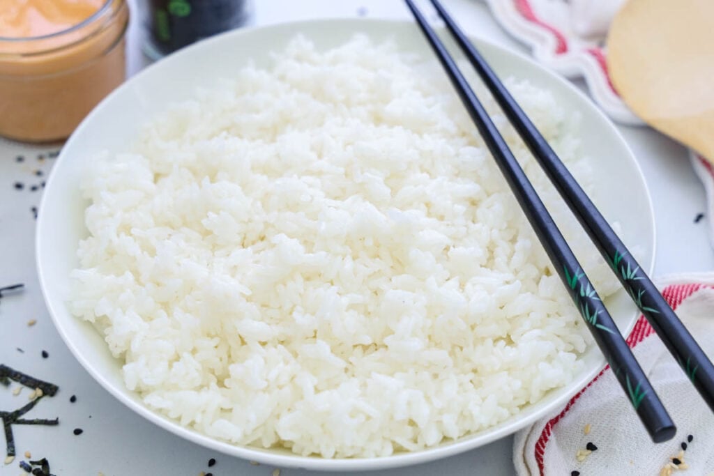 A bowl of Sushi Rice with a pair of chopsticks on the edge.