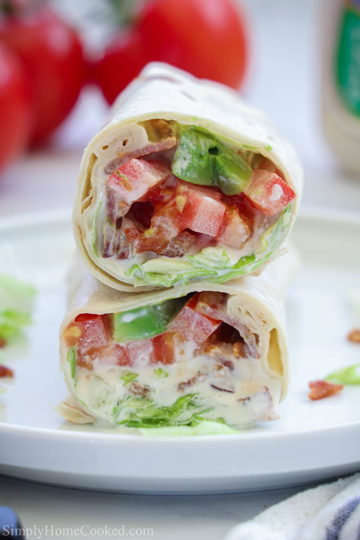 Two halves of an Easy BLT Wrap stacked on top of each other on a white plate.