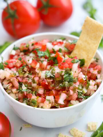Pico de Gallo in a white bowl with a tortilla strip in it