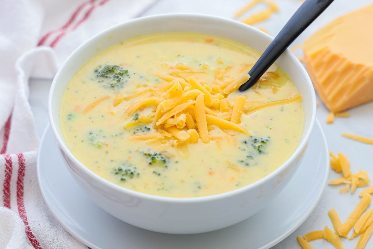 Bowl of Broccoli Cheddar Soup with cheese on top and a spoon in it.