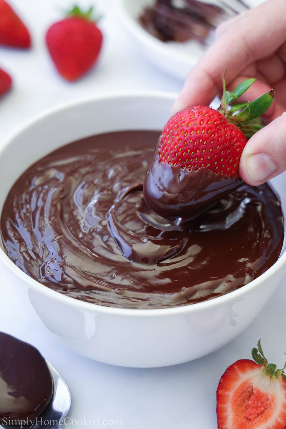 Learn how to make this delicious chocolate ganache. This ganache recipe can be used in a large variety of desserts to give it that final touch of flavor. #chocolateganache #chocolateglaze #ganache #mirrorglaze #smoothchocolate Hand dipping a strawberry into a bowl of Chocolate Ganache