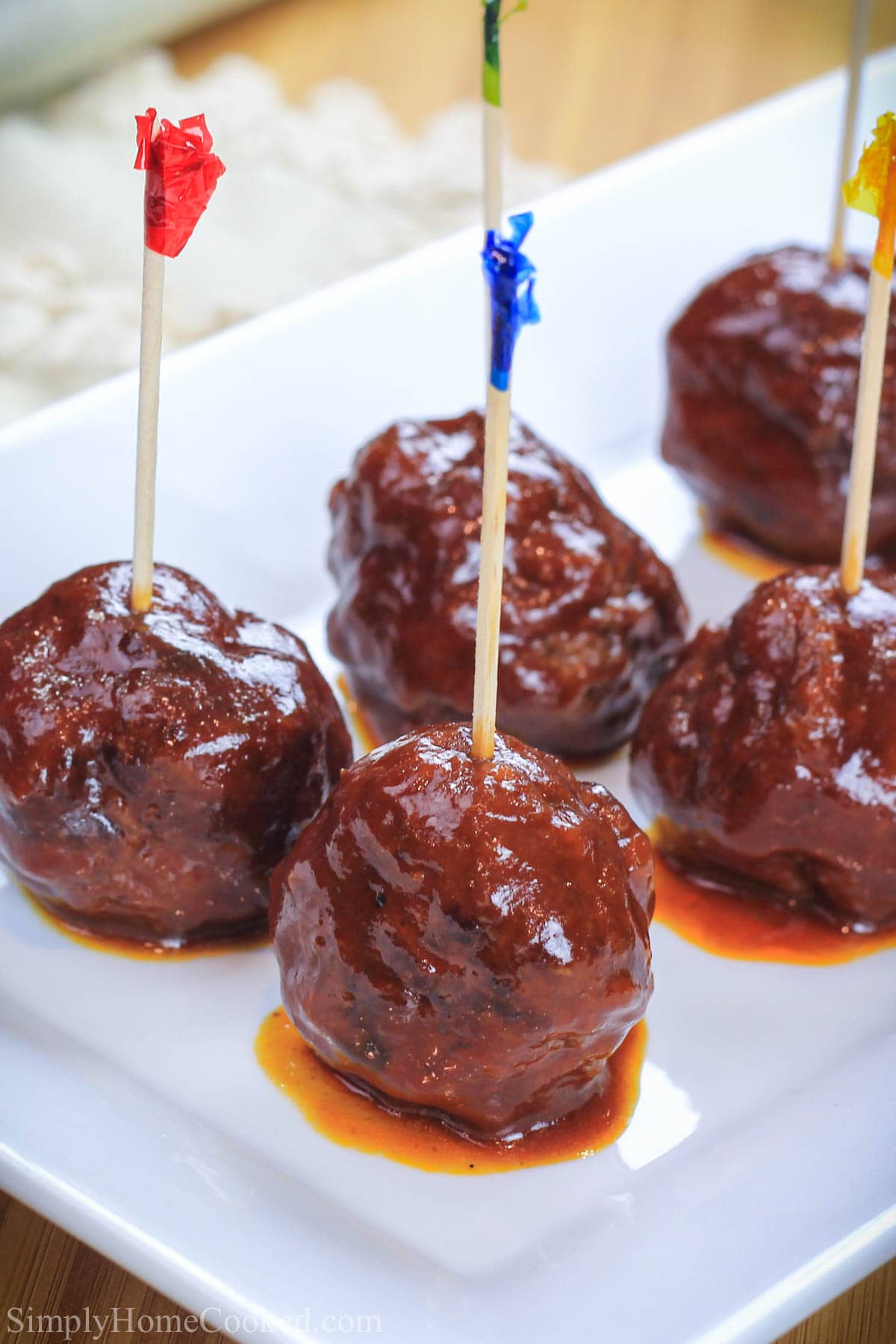 Homemade Barbecue Meatballs are the perfect appetizer featuring simple ingredients and a delightful homemade sauce that is ideal for parties and events. #meatballs #bbqmeatballs #bestmeatballs #grilledmeatballs #superbowlmeatballs #barbecuemeatballs Grilled BBQ Meatballs with toothpicks in them on a white plate.
