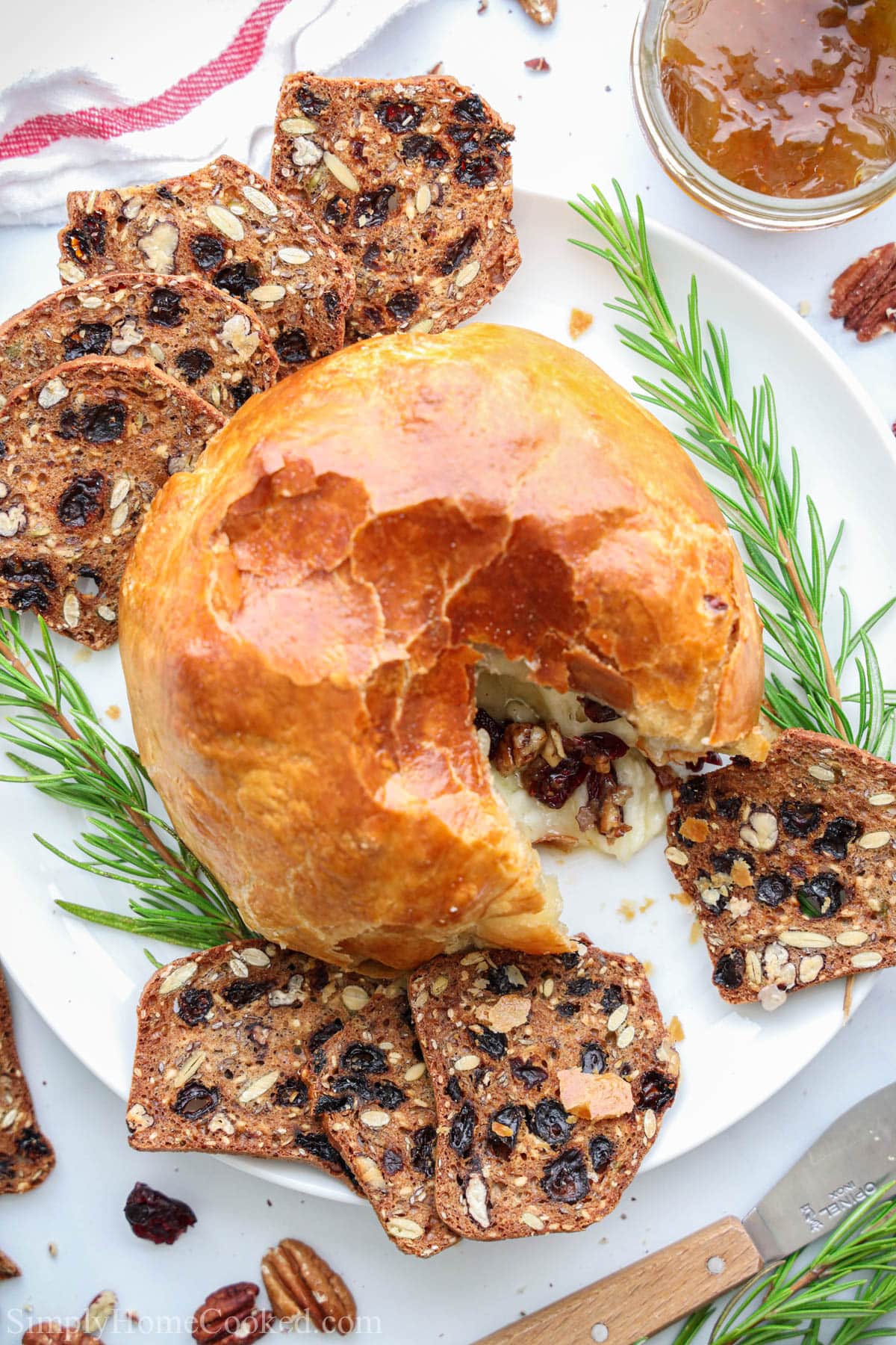 Baked Brie in Puff Pastry on a white plate with rosemary sprigs and bread slices.
