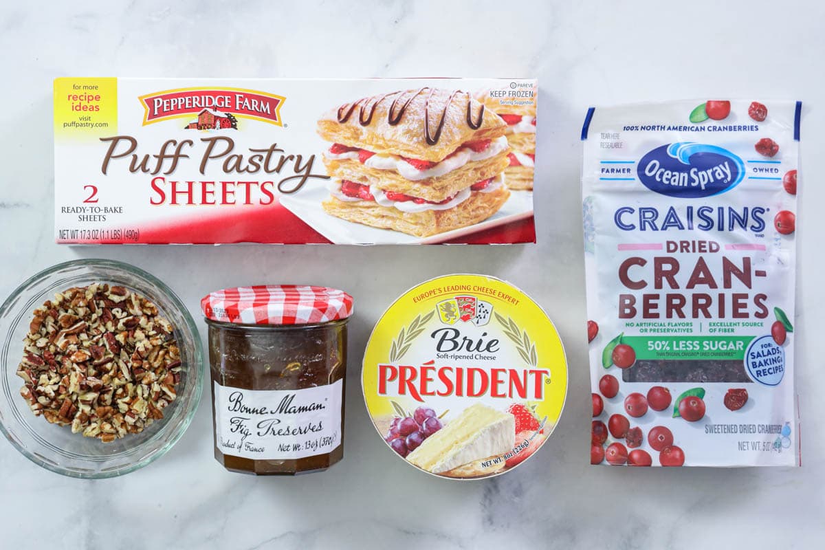 Ingredients for Baked Brie in Puff Pastry: puff pastry sheets, cranberries, brie cheese, fig jam, and pecans.