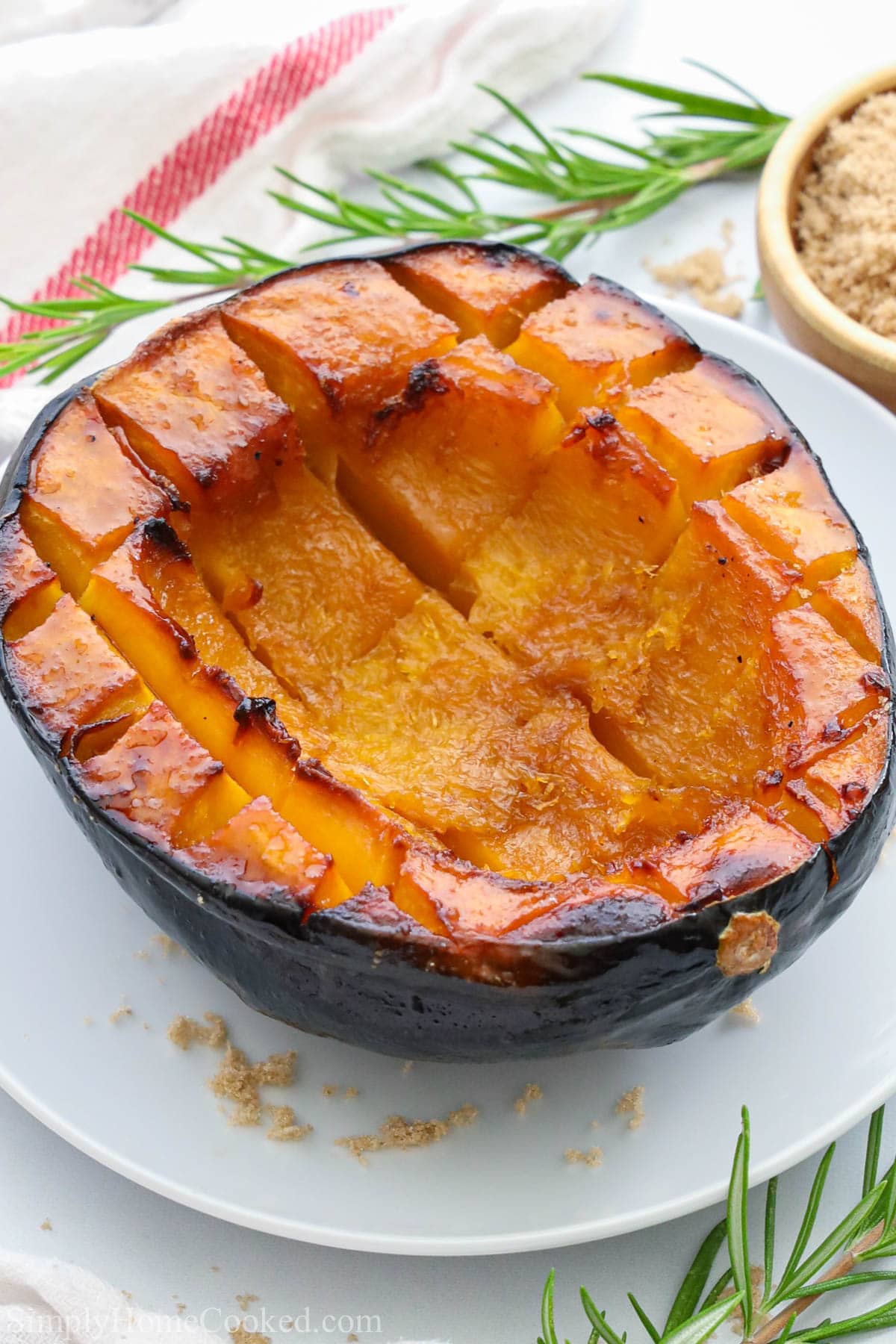 Roasted Acorn Squash on a white plate with brown sugar nearby.