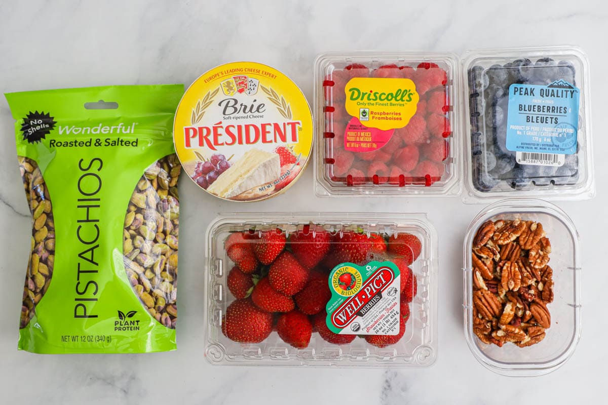 Ingredients for Dessert Charcuterie Board: pistachios, pecans, strawberries, blueberries, raspberries, and brie cheese.
