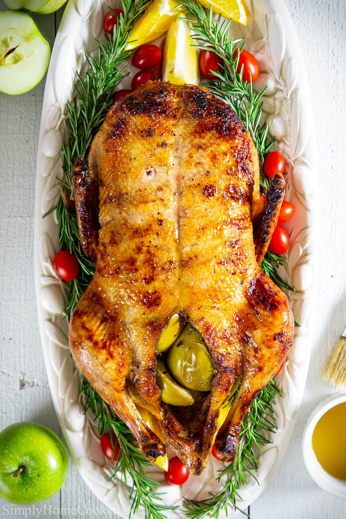 This easy roast duck recipe is so juicy, tender, and so flavorful. And the zesty orange glaze gives the golden crispy skin perfect sweetness! #roastduck #duckroast #holidayduck #dinnerduck #stuffedduck Roast Duck stuffed with apples on a white platter.