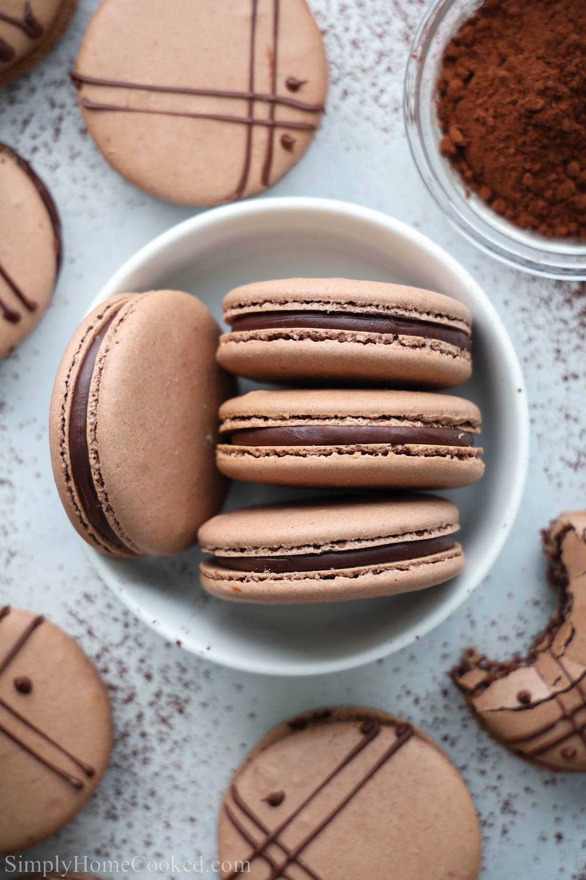 Chocolate Macarons with a ganache filling in a bowl with others scattered nearby.