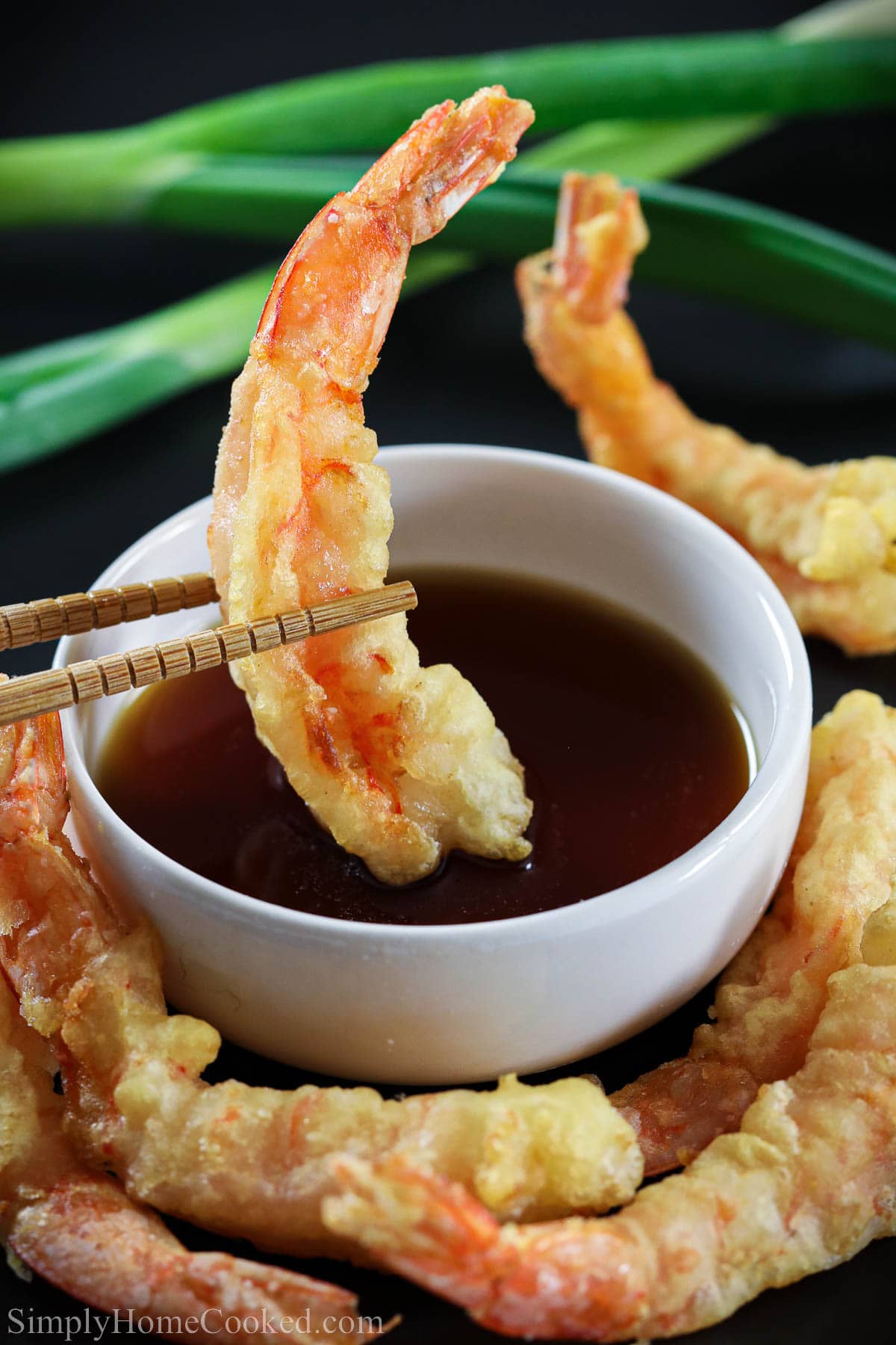 This Shrimp Tempura Dipping Sauce is sweet, salty, and savory. It really complements the delicate flavors of your vegetable or shrimp tempura. #dippingsauce #tempuradippingsauce #shrimptempurasauce #dippingsaucerecipe Shrimp Tempura being dipped into Tempura Dipping Sauce in a white bowl with chopsticks.