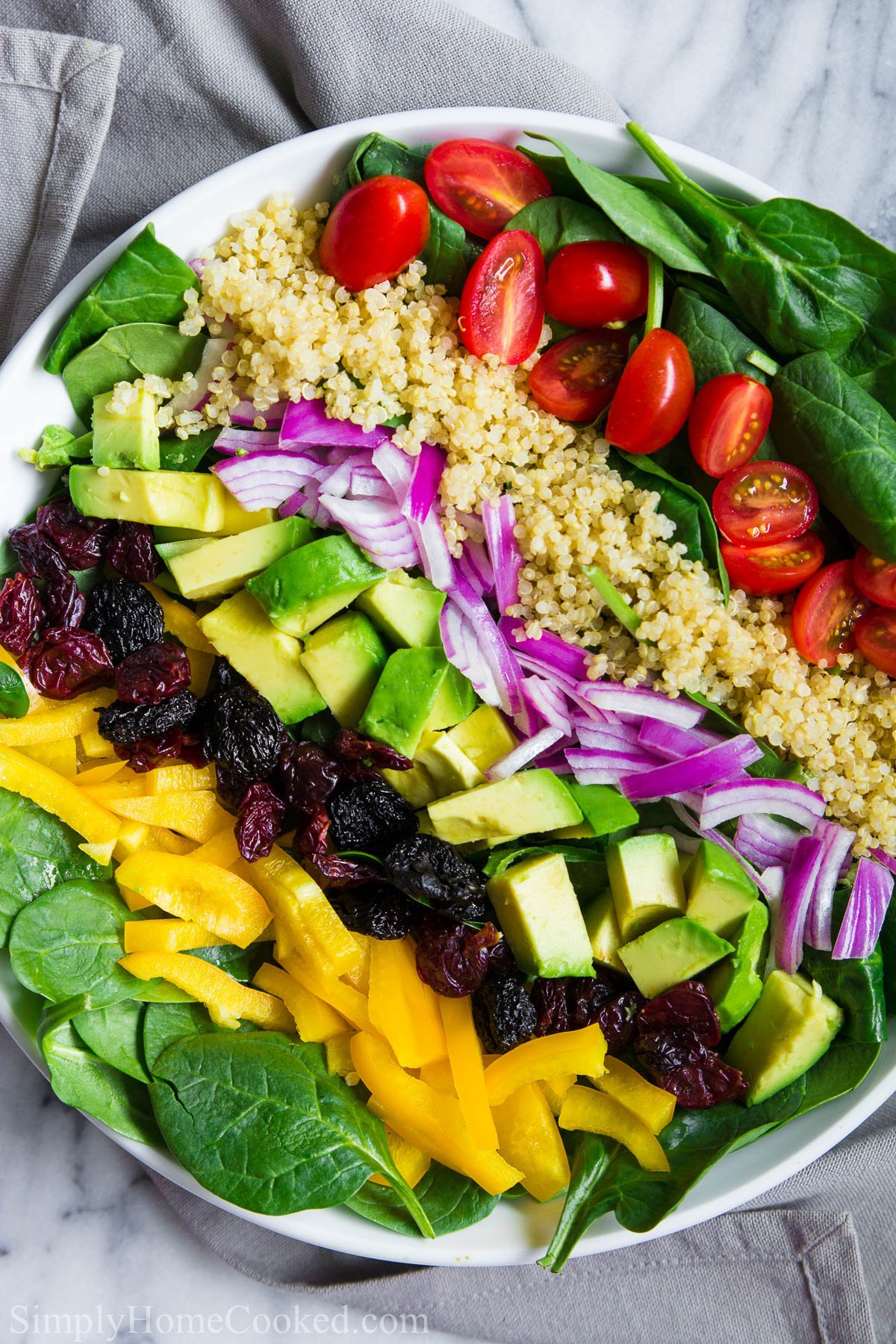 This simple Spinach salad is loaded with crisp spinach, creamy avocado, and juicy cherry tomatoes and its tossed in an incredible Greek salad dressing. #spinachsalad #healthysalad #spinach #saladrecipe #saladdressing A Spinach Salad topped with cherry tomatoes, red onion, avocado, bell pepper, dried cherries, and cooked quinoa,