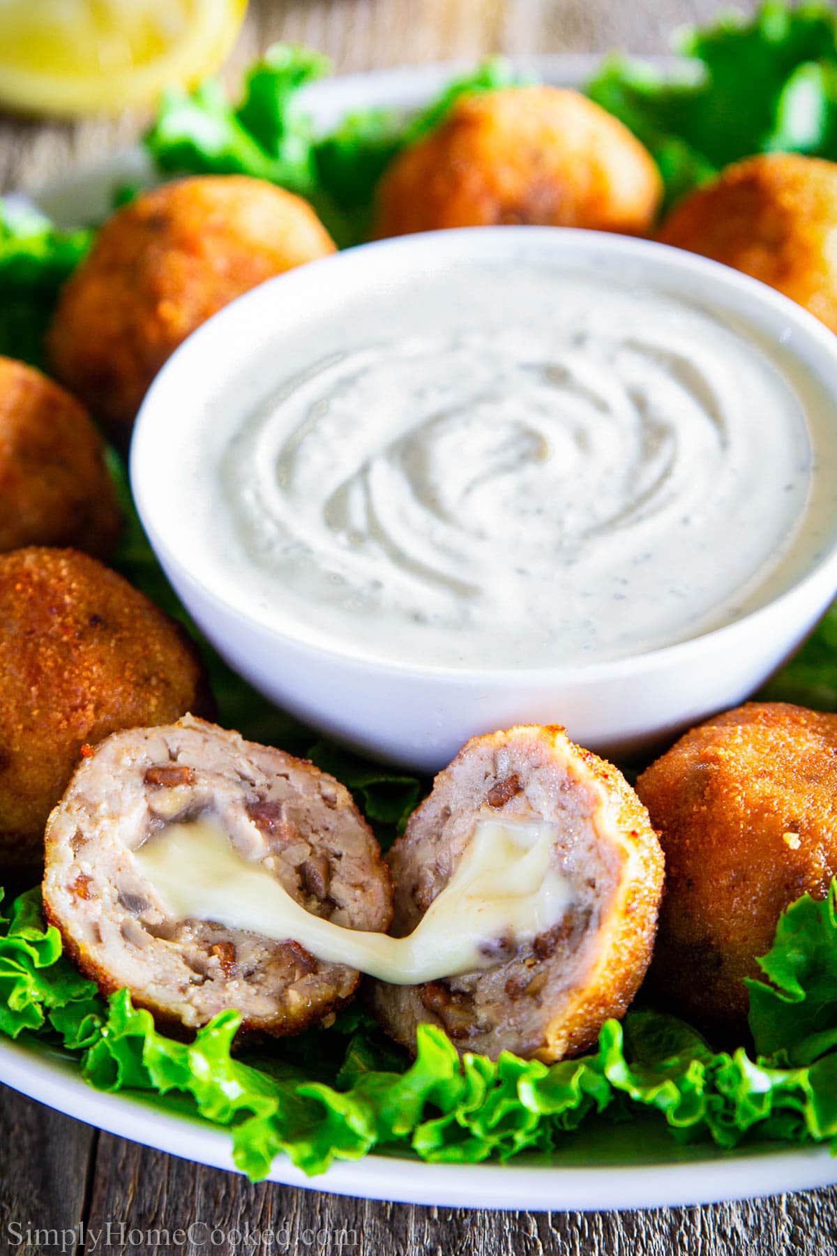 This Chicken Croquettes recipe is that one appetizer filled with cheese and a crunchy coating and cheesy filling that will disappear in seconds! #croquettes #chickencroquettes #cheesemeatballs #stuffedmeatballs #chickenmeatballs #friedmeatballs Chicken Croquettes around a bowl of ranch dressing, one split in half to show the gooey cheese.
