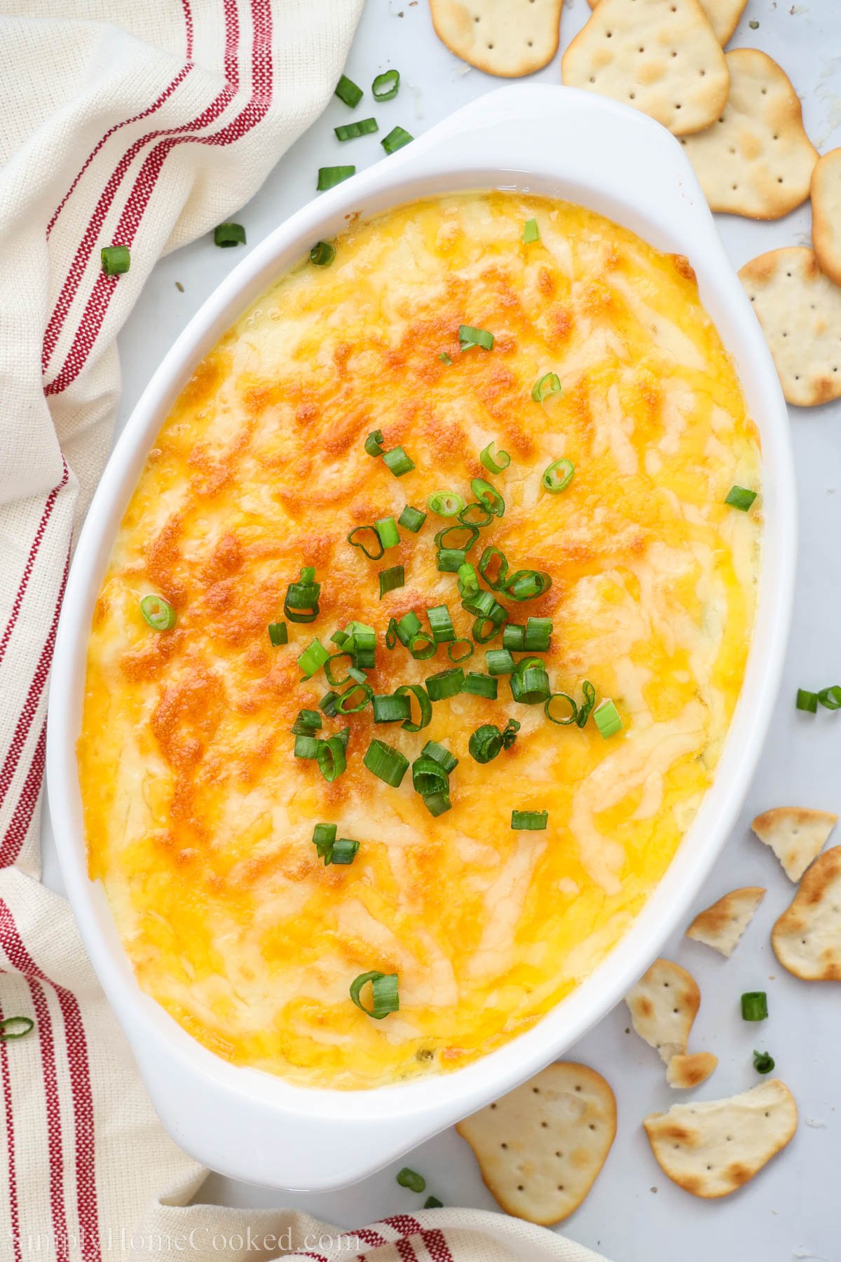 Crab Artichoke Dip in a serving dish topped with cheese and green onion with crackers nearby.