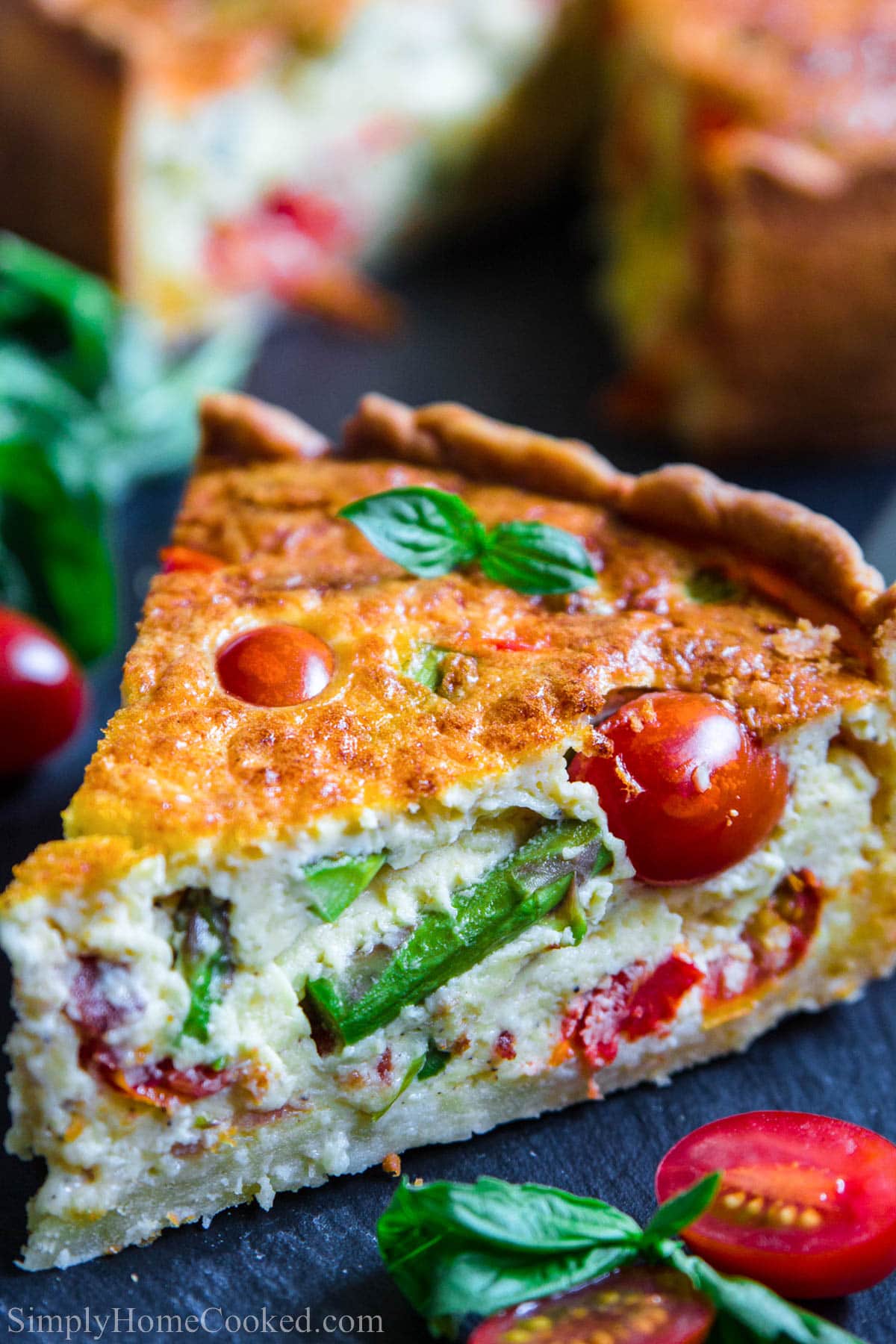 This Quiche Lorraine recipe is a scrumptious combination of flakey buttery crust filled with fresh spring vegetables, bacon, cheese, and eggs. #quiche #quicheLorraine #lorraine #quicherecipe #breakfastpie #savorypie Slice of Quiche Lorraine with asparagus and cherry tomatoes.