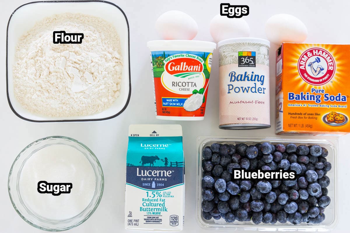 Ingredients for Blueberry Ricotta Pancakes: flour, sugar, baking powder, baking soda, ricotta cheese, eggs, blueberries, and buttermilk.