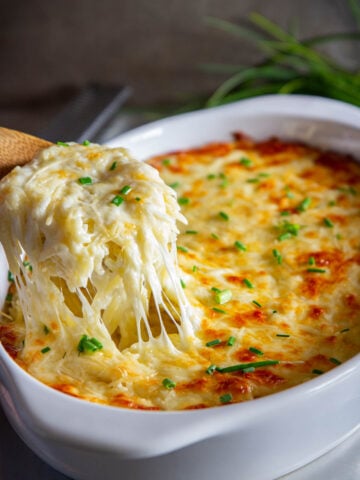 Baking dish of Creamy Orzo sprinkled with chopped chives, a spoonful being lifted out.